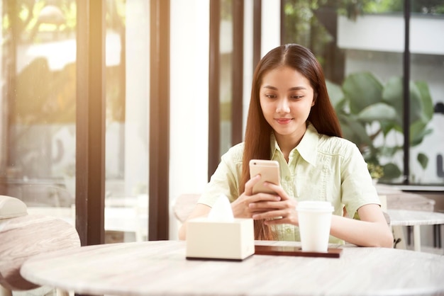 Donna asiatica con caffè sul tavolo usando un telefono cellulare nella caffetteria