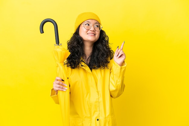 Donna asiatica con cappotto antipioggia e ombrello isolato su sfondo giallo che indica una grande idea