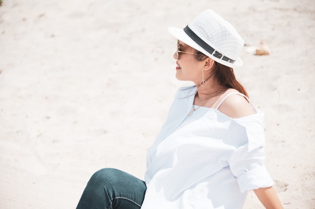 Donna asiatica con la camicia bianca che si distende sulla spiaggia, ora legale