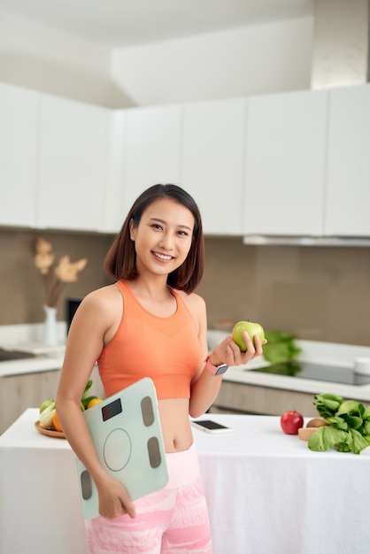 Donna asiatica con mela e bilancia in cucina