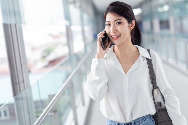 Donna asiatica con smartphone che cammina sullo sfondo di un edificio sfocato strada Affari di moda