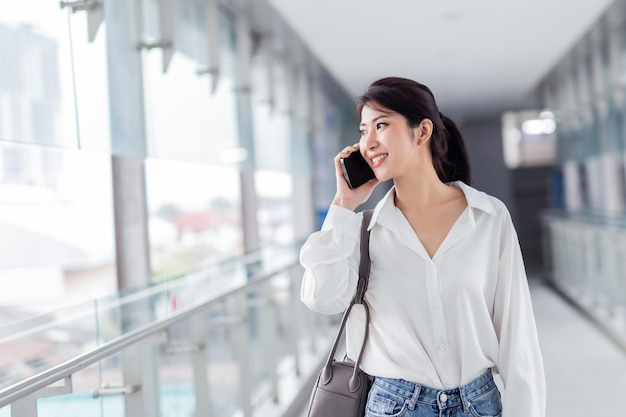 Donna asiatica con smartphone che cammina sullo sfondo di un edificio sfocato strada Affari di moda