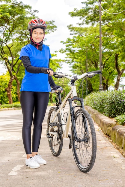 Donna asiatica con un casco in piedi accanto alla sua bicicletta