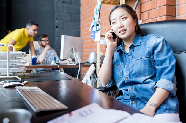 Donna asiatica contemporanea che parla dal telefono sul lavoro