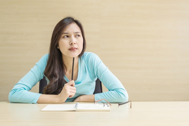 Donna asiatica del primo piano che lavora con l&#39;emozione del fronte di pensiero e una matita in sua mano