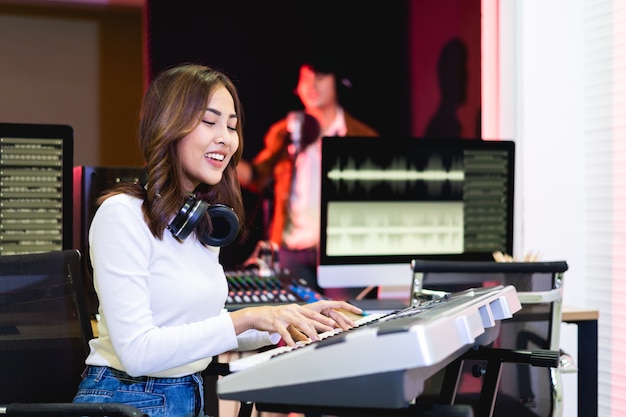 Donna asiatica del produttore in camicia bianca che fa una pausa la console di missaggio del suono. Felice compositrice di musica femminile con un background da cantante maschile