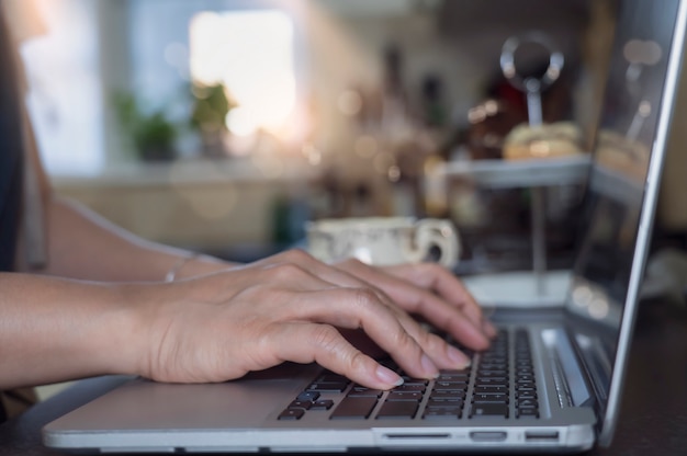 Donna asiatica di affari che utilizza computer portatile che funziona nella cucina