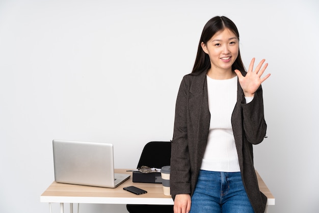 Donna asiatica di affari nel suo posto di lavoro sulla parete bianca che conta cinque con le dita