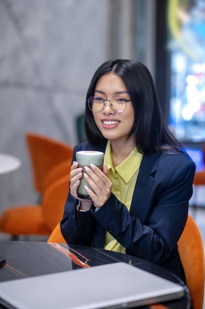 Donna asiatica di affari nell'ufficio che mangia il caffè del mattino