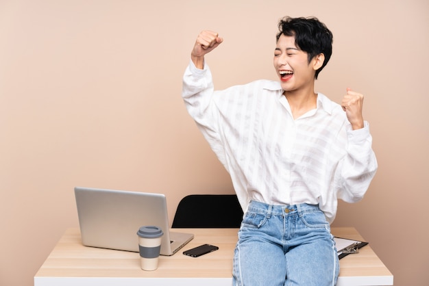 Donna asiatica di giovani affari nel suo luogo di lavoro che celebra una vittoria