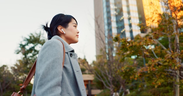 Donna asiatica e cuffie viaggiano in città e si recano al lavoro con la radio o il podcast all'aperto Tecnologia girare e ascoltare musica in viaggio strada urbana e professionalmente camminare all'aperno