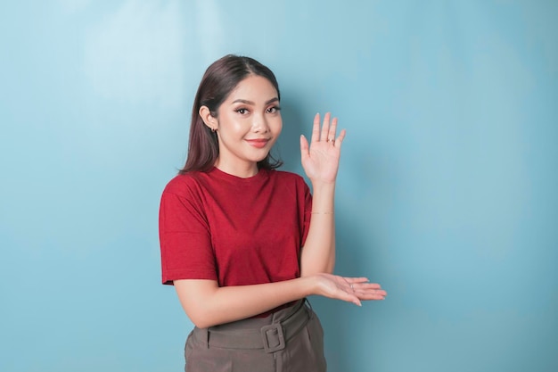 Donna asiatica eccitata che indossa una maglietta rossa che punta allo spazio della copia accanto a lei isolato da sfondo blu