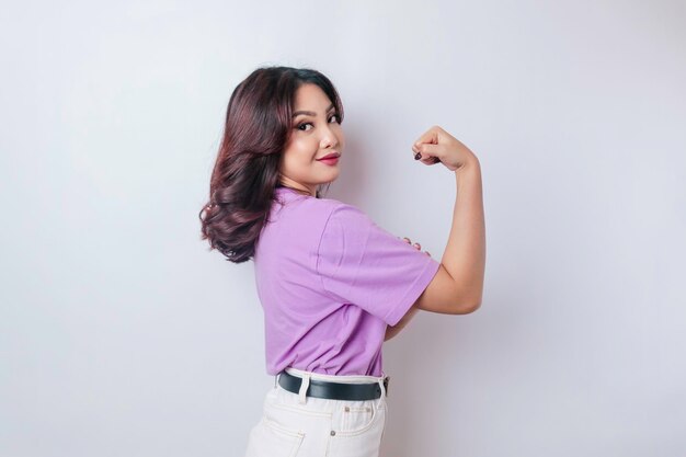 Donna asiatica eccitata che indossa una maglietta viola lilla che mostra un gesto forte sollevando le braccia e i muscoli sorridendo con orgoglio