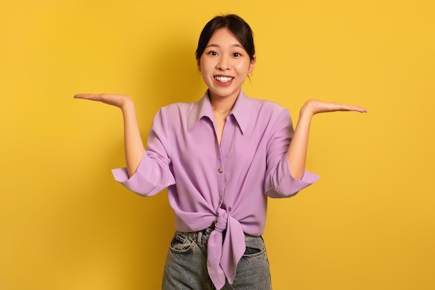 Donna asiatica felice che confronta le opzioni che fanno le scale con le mani che tengono oggetti invisibili su giallo