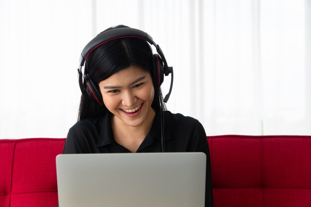 Donna asiatica felice che si siede su un sofà e su una videoconferenza con un socio commerciale su un computer portatile