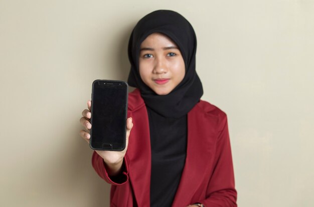 Donna asiatica felice di affari in hijab che dimostra telefono cellulare mobile. Ritratto di donna sorridente, in posa