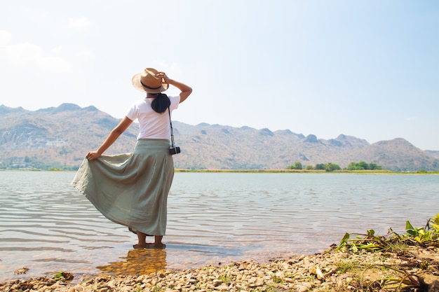 Donna asiatica felice in vestiti di stile casuale che si levano in piedi nel fiume con il Mountain View su priorità bassa