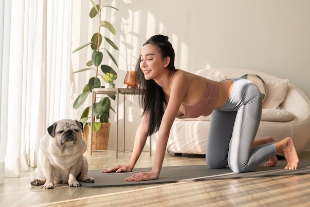 Donna asiatica in abbigliamento sportivo che si esercita e fa yoga con un cane carino nel salotto di casa