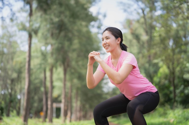 Donna asiatica in abbigliamento sportivo rosa che fa esercizi di squat nel parkxDxA