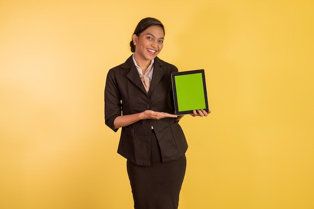 Donna asiatica in abito formale che mostra e indica il tablet digitale con schermo verde su arancione