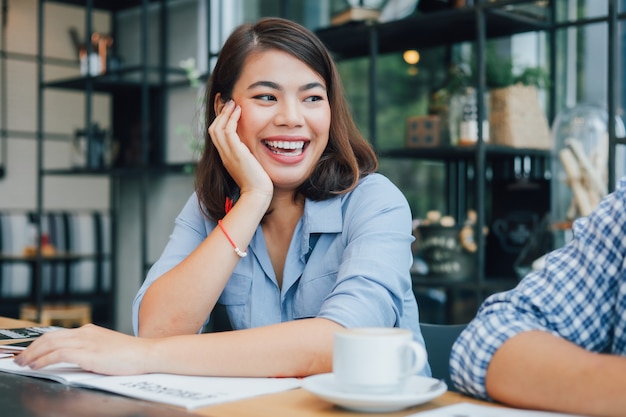 Donna asiatica in camicia blu nel caffè bevente del caffè e parlare con il sorriso dell'amico e il fronte felice