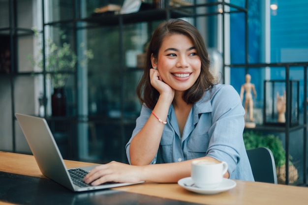 Donna asiatica in camicia blu nel caffè bevente del caffè e parlare con il sorriso dell'amico e il fronte felice