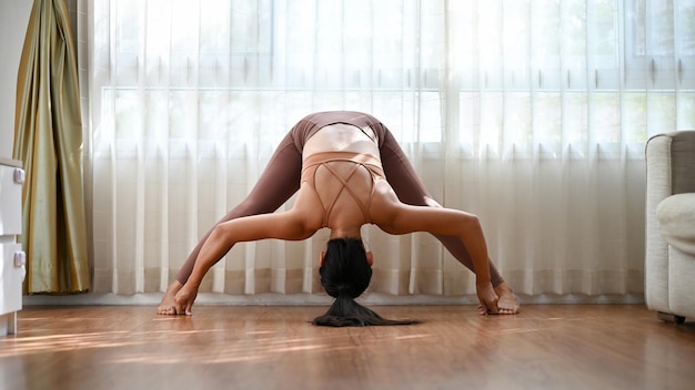 Donna asiatica in forma sana che pratica yoga a casa Gamba larga piega in avanti posa D