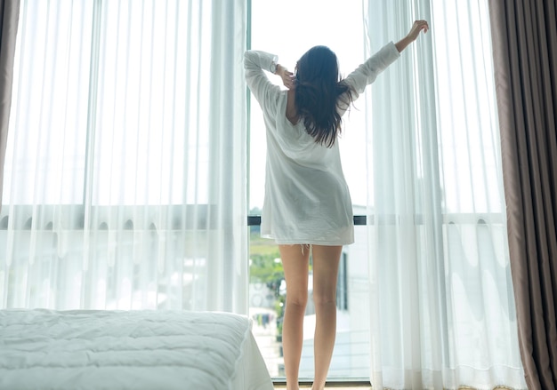 Donna asiatica in piedi vicino alla finestra e stretching al mattino