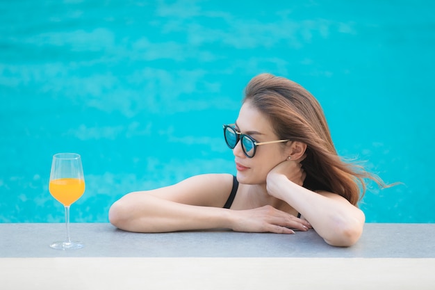 Donna asiatica in piscina con un bicchiere di succo d&#39;arancia