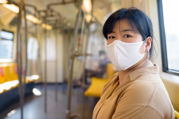 Donna asiatica in sovrappeso con maschera seduta con la distanza all'interno del treno