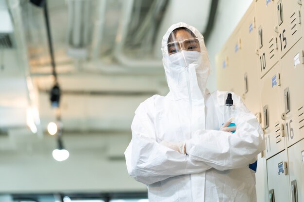 Donna asiatica in tuta protettiva e maschera per la disinfezione in ufficio. Protezione contro la malattia COVID-19