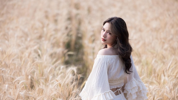 Donna asiatica in un campo di grano Ritratto bella donna nel campo di grano sorridente Belle donne asiatiche in abito bianco a piedi campi d'orzo d'oro