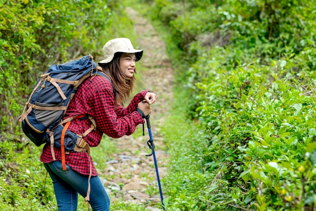 Donna asiatica in un cappello e zaino con un bastone da trekking a piedi stanchi