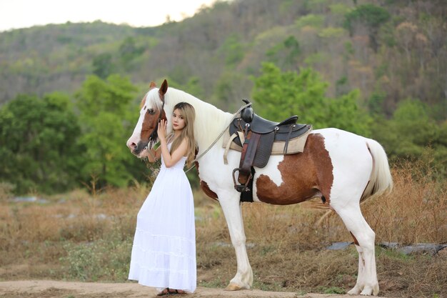 Donna asiatica in un costume abito lungo sta con un cavallo in un allevamento di bestiame.