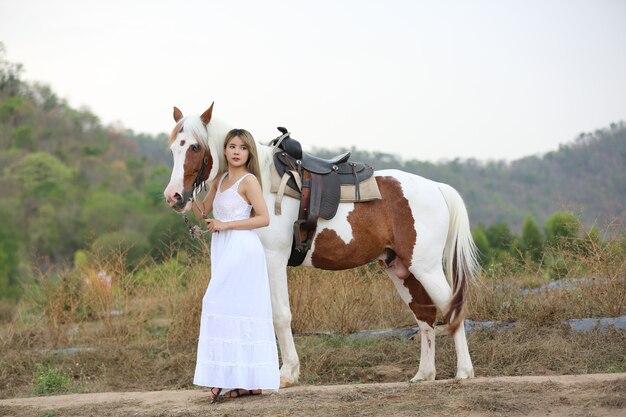 Donna asiatica in un costume abito lungo sta con un cavallo in un allevamento di bestiame.