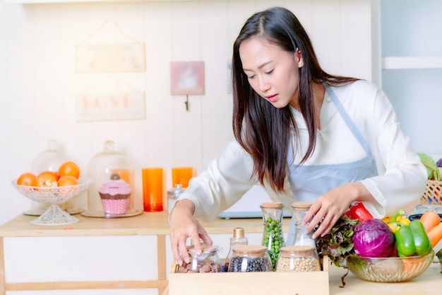 Donna asiatica in un grembiule che cucina alimento sano nella cucina.