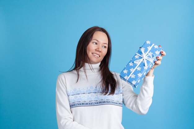 Donna asiatica in un maglione guardando un regalo blu