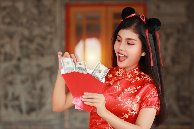 Donna asiatica in vestito cinese rosso qipao tradizionale cheongsam con gesto di apertura della busta rossa con i soldi