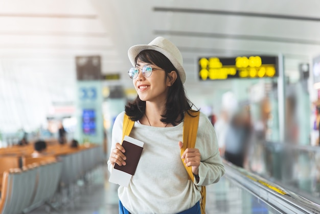 Donna asiatica indossare occhiali, cappello con zaino giallo è in possesso di biglietto di volo, passaporto presso la hall dell'aeroporto.