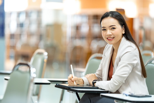 Donna asiatica Insegnante che prende appunti dal tablet in biblioteca all'università