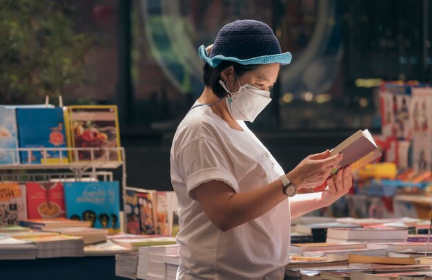 Donna asiatica plus size in maschera protettiva che sceglie libro al negozio di libri nell'area del centro commerciale