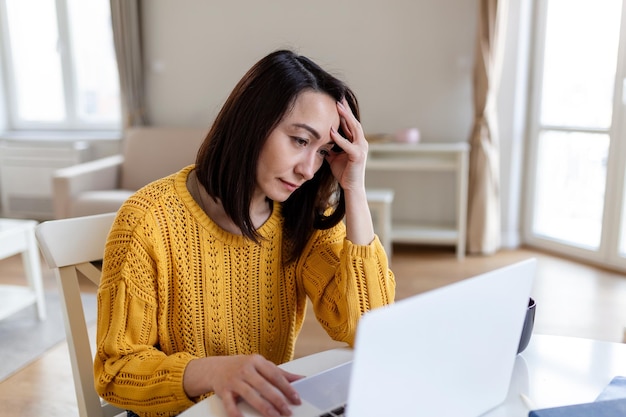 Donna asiatica preoccupata di pensare al problema online Donna di mezza età frustrata e preoccupata che soffre di perdita di memoria con mal di testa