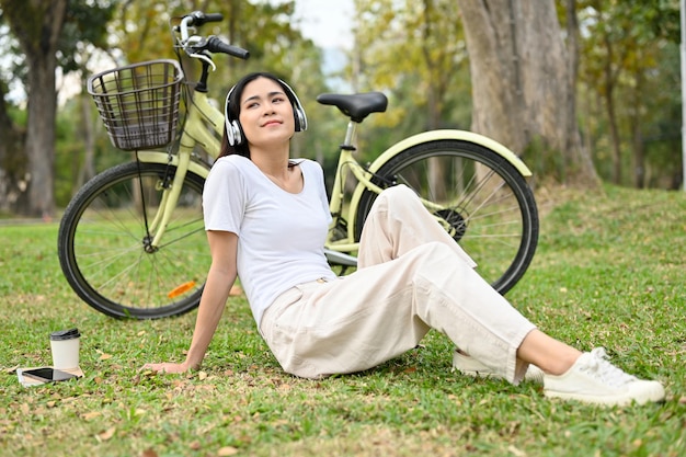 Donna asiatica rilassata che ascolta musica e si riposa dopo aver pedalato nel parco pubblico