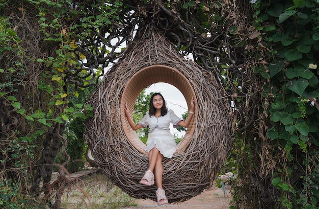Donna asiatica seduta in un nido di uccelli in legno nella foresta di alberi verdi che guarda lontano felice con la natura