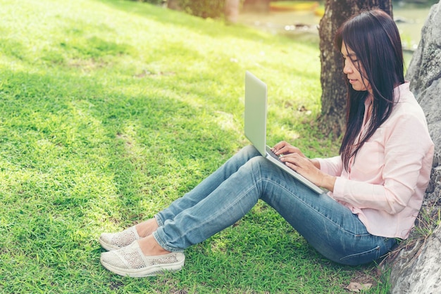 Donna asiatica seduta nel parco verde utilizzando un computer portatile Donna che lavora su un computer portatile felice imprenditore utilizzando il notebook con le mani che digitano sulla tastiera dell'ufficio a casa durante il periodo di quarantena del coronavirus