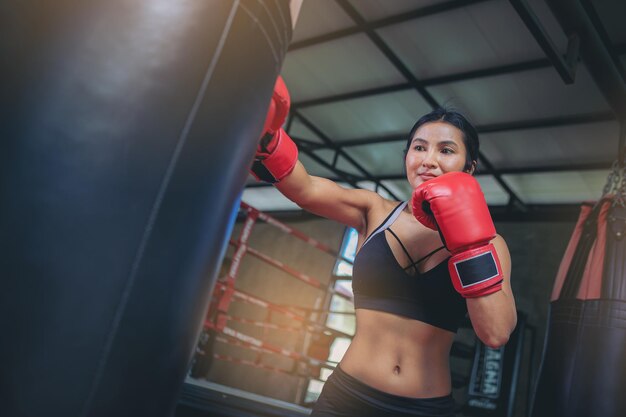 Donna asiatica sexy che fa esercizio di allenamento facendo pugilato con un sacco di sabbia in palestra. Messa a fuoco selezionata