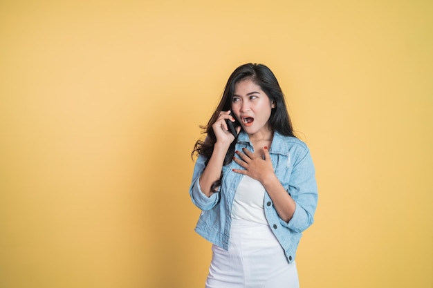 Donna asiatica sorpresa che effettua una chiamata utilizzando un telefono cellulare