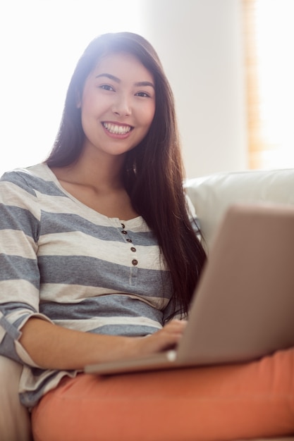 Donna asiatica sorridente che per mezzo del computer portatile sullo strato
