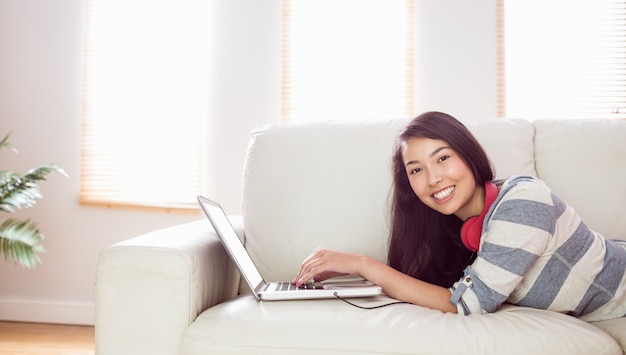 Donna asiatica sorridente sullo strato facendo uso del computer portatile