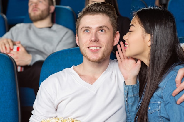 donna asiatica sussurrando al suo allegro ragazzo sorridente mentre si guarda un film commedia al cinema